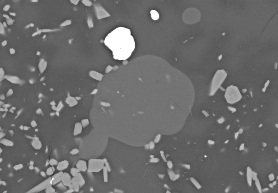 Backscattered-electron image of a quenched experiment: a round carbonate droplet in silicate glass among small crystals
